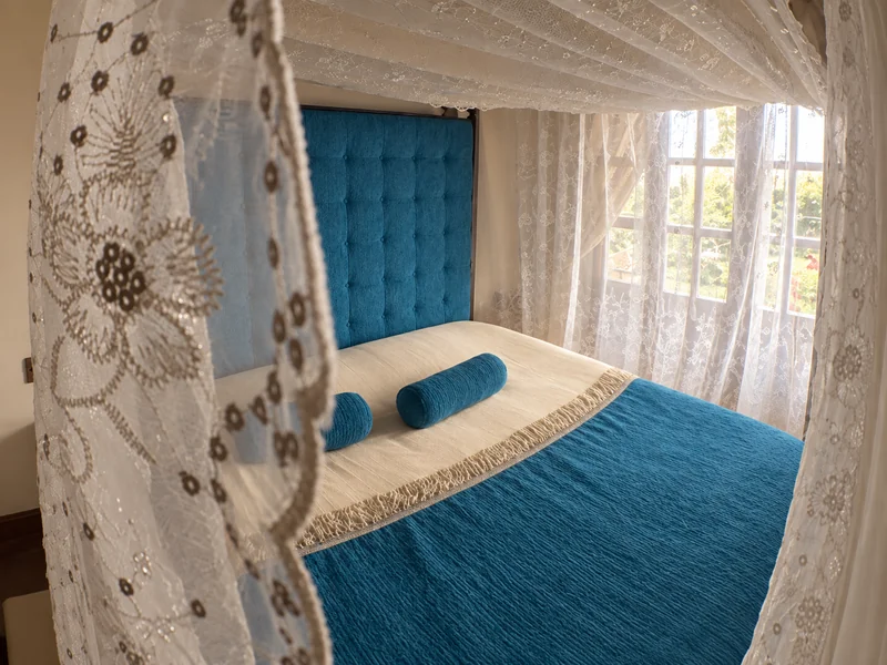 Cama con toldillo blanco y cubrelecho azul en una de las unidades